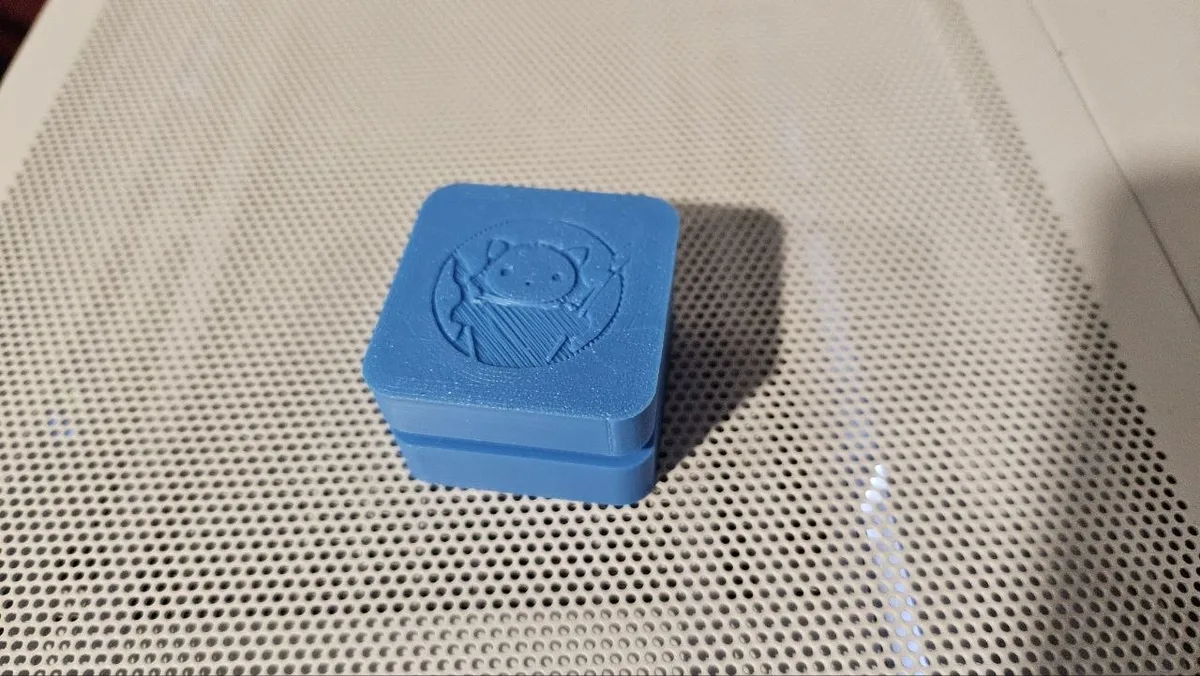 Clicker cuadrado redondeado impreso en 3D en PLA azul con la imagen de un gato grabada en la tapa