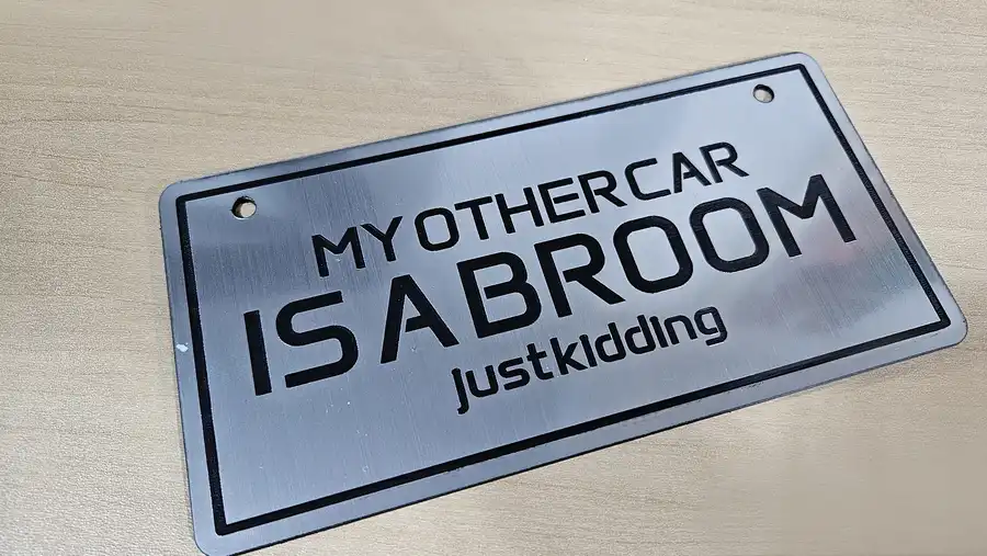 Brushed chrome acrylic novelty plate reading MY OTHER CAR IS A BROOM just kidding with black engraving