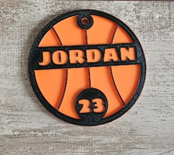 Etiqueta de baloncesto para bolsa impresa en 3D en PLA naranja y negro con el nombre JORDAN y el número 23