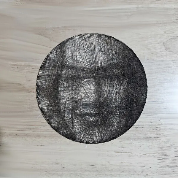 String art portrait laser-cut on a round maple plywood disc, threaded with dark string between edge pegs