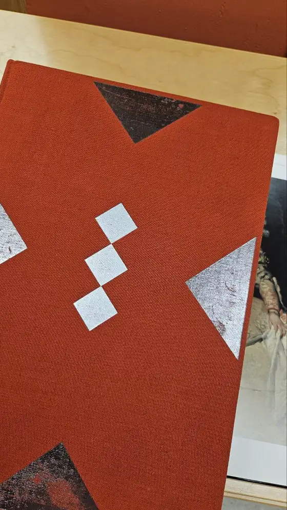 Un libro encuadernado en tela rojo óxido con ornamento geométrico plateado en la cubierta