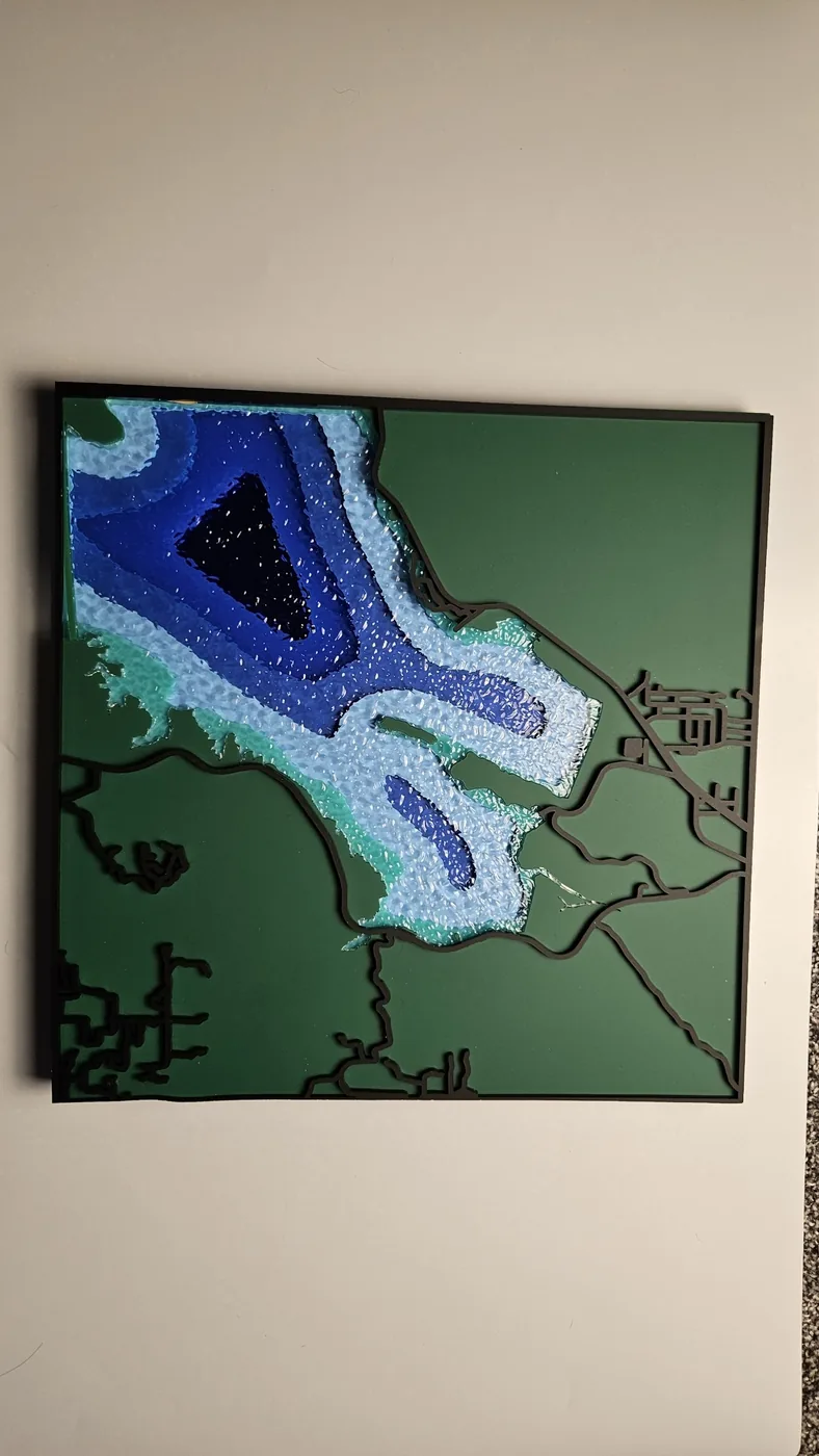 Una carta de profundidad de una ensenada cortada a láser con franjas de agua azules por capas sobre un panel verde