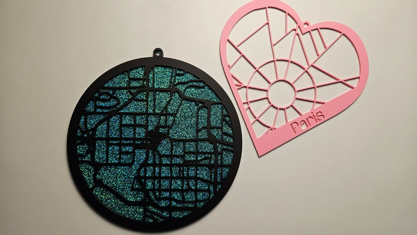 Un adorno redondo con un mapa urbano en acrílico con purpurina junto a un mapa de París en forma de corazón rosa