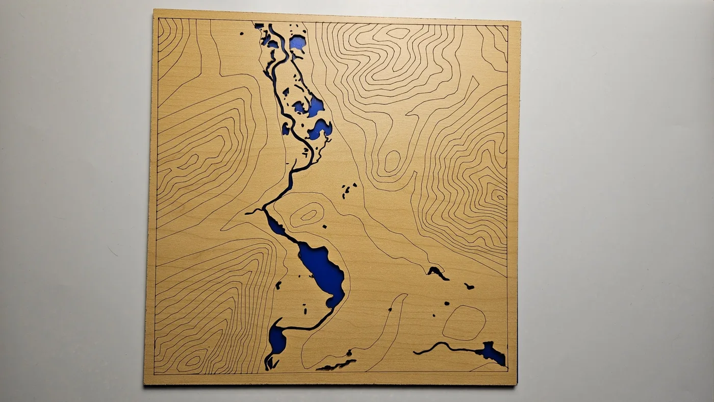 Un panel de madera con curvas de nivel marcadas y un río azul cortado a través de él