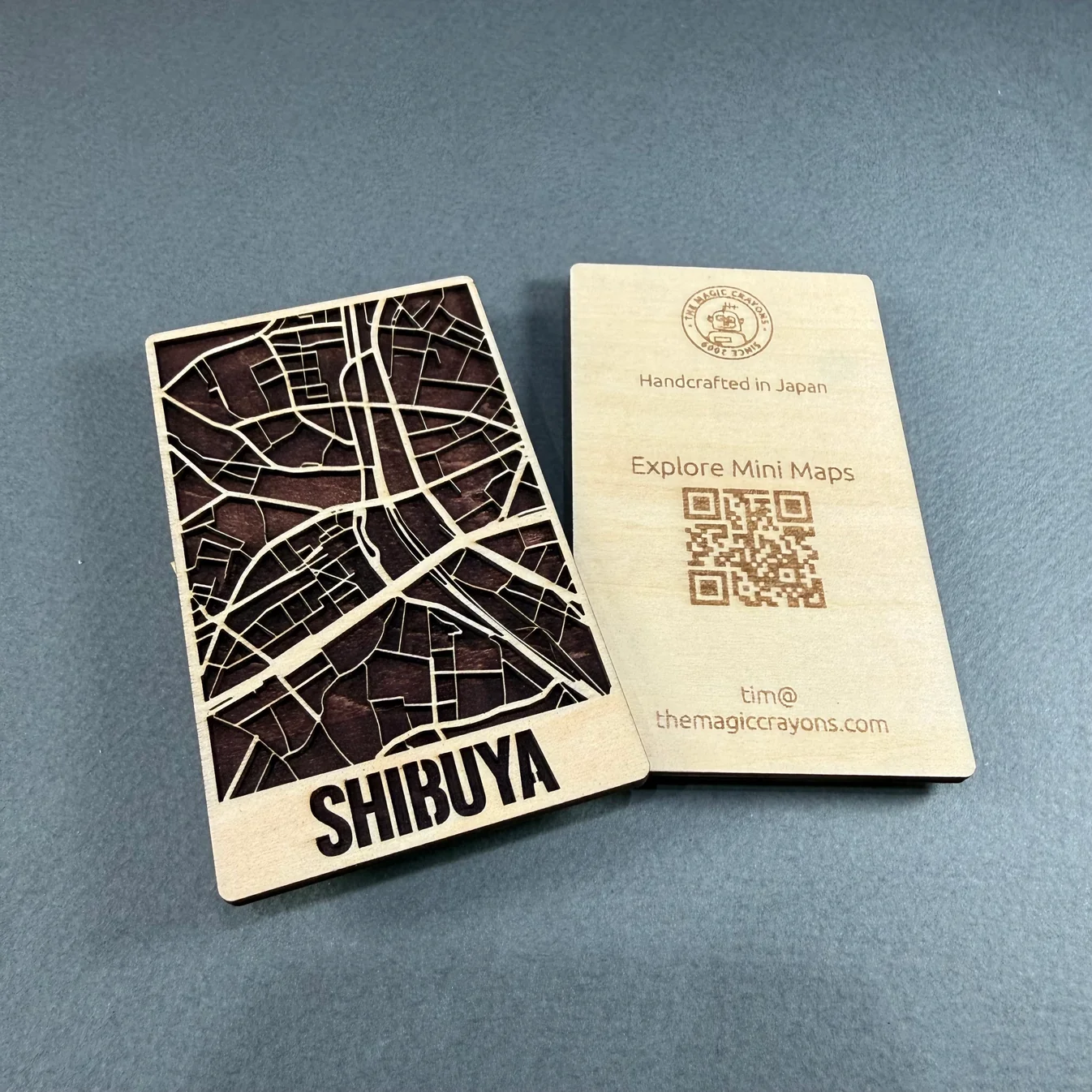 Pocket-sized Shibuya mini map cut from birch ply with a dark stained street layer, shown front and back alongside the engraved Magic Crayons card, made with the MyLaserTools map generator.