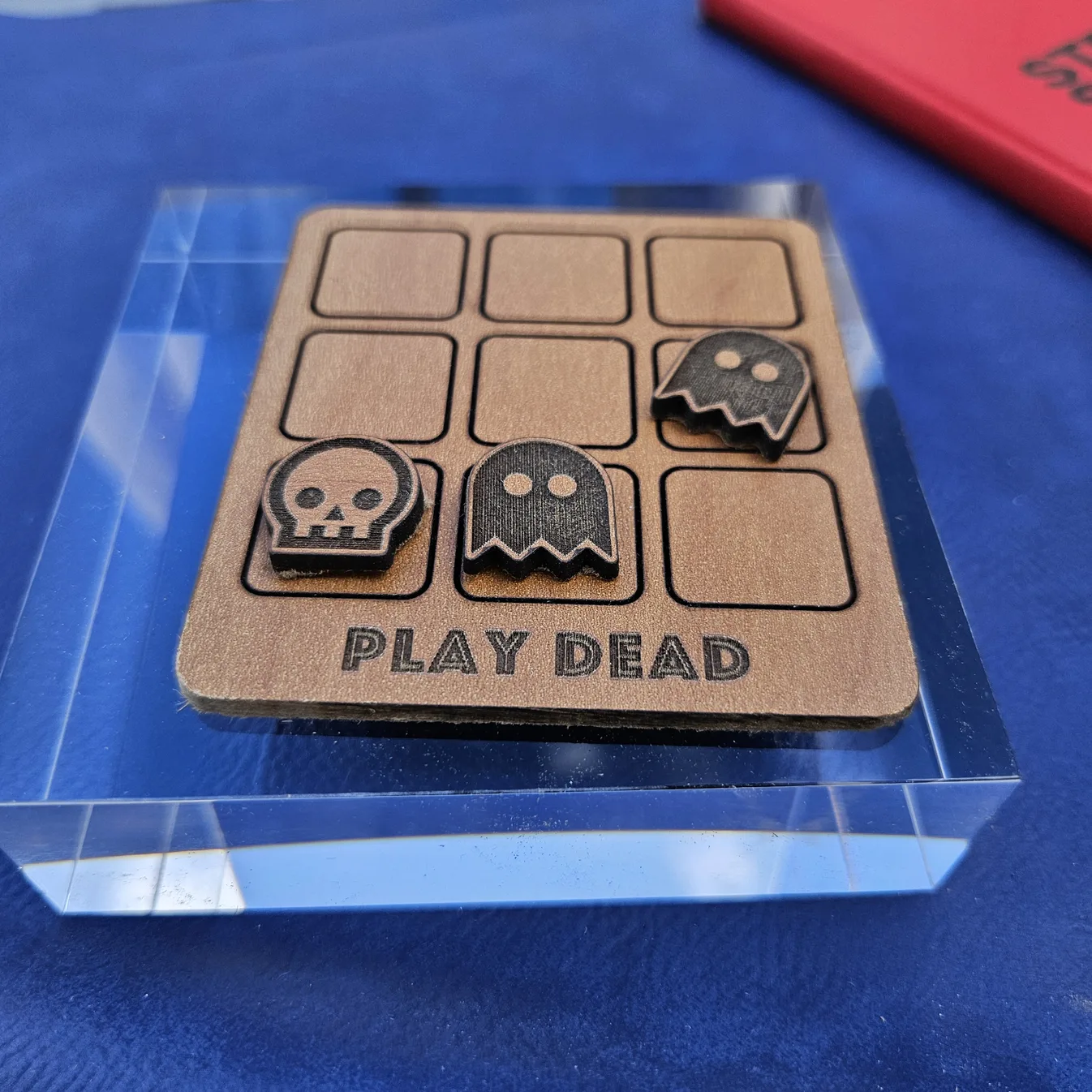 Laser-cut wooden Play Dead tic-tac-toe board by Sofia Reyker, with ghost and skull game pieces and engraved lettering, made with MyLaserTools.