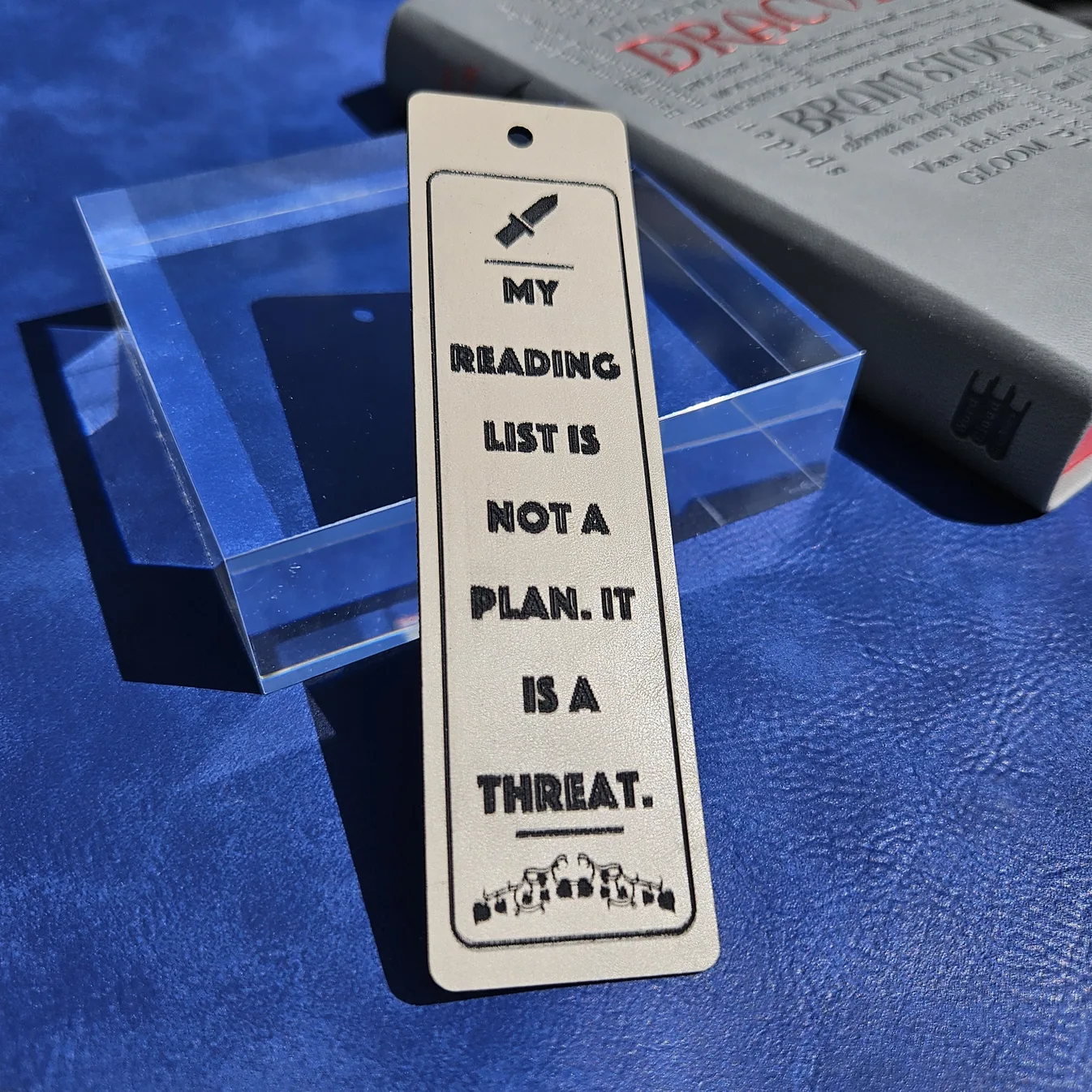 Engraved wooden bookmark reading "My reading list is not a plan, it is a threat," with knife and stacked-book icons, made by Sofia Reyker with MyLaserTools.